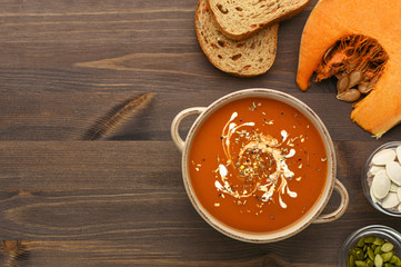 Pumpkin soup puree decorated with cream on wood background top view. Vegetables bread, pumpkin and seeds on wooden background with place for text. Copy space. Menu, recipe, thanksgiving day. 