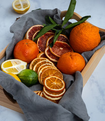 Side view of a wooden basket with fresh oranges and dried oranges on a gray background