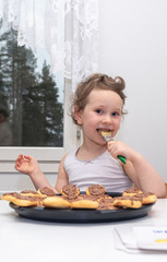 Child European girl baked homemade cookies6 sitting in the kitchen. Lubricates cookies with liquid chocolate