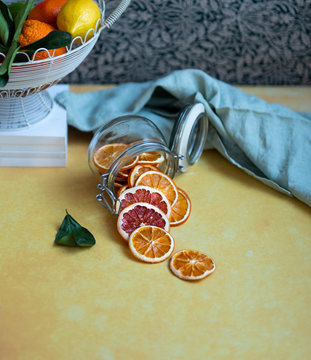 Side view of a jar overturned with slices of dried orange and grapefruit on a yellow background