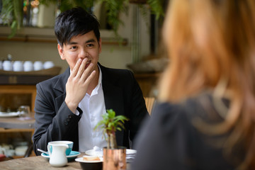 Young Asian business couple together at the coffee shop with man looking shocked
