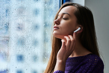 Young woman music lover with closed eyes in wireless earbuds enjoys and listens to soothing calming...