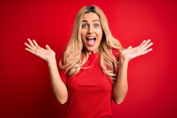 Young beautiful blonde woman wearing casual t-shirt standing over isolated red background...