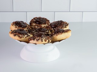 Raised white platter display with thumbprint cookies coated in chocolate frosting and sprinkles on a white counter with a white subway tile background.  Delicious baked goods.