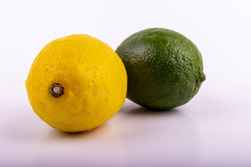 One delicious and sour yellow lemon and one green lime lie on a table against a white background.