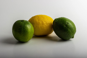 Two delicious and sour green limes and one yellow lemon lie on a table against a white background.
