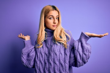 Young beautiful blonde woman wearing casual turtleneck sweater over purple background clueless and...