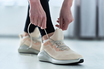 Fitness athletic woman ties shoelaces on beige comfortable sneakers and get ready for jogging and workout. Do sport and be fit. Sports people with healthy sporty lifestyle
