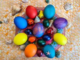 Fototapeta na wymiar Religious Easter holiday, on an orange grid lies a plate with multi-colored chicken and quail eggs, sea shells and shells are laid around them.