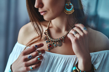 Stylish brunette boho woman wearing white blouse with big earrings, necklace with stone and silver...