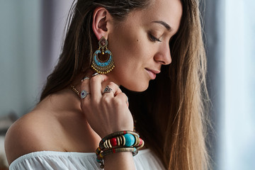 Stylish sensual brunette boho chic woman wears big earrings, bracelet with stone and silver rings....