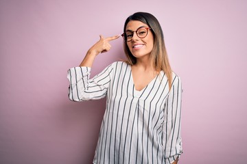 Young beautiful woman wearing casual striped t-shirt and glasses over pink background Smiling pointing to head with one finger, great idea or thought, good memory