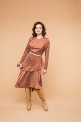 Beautiful young female with short dark hair, pretty face in long orange dress, ocher color long boots smiles