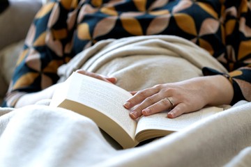 A portrait of a person fallen asleep under a blanket while reading a book. The hand of the person...