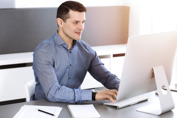 Businessman working with computer in modern sunny office. Headshot of male entrepreneur or company...