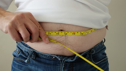 Front Of Overweight Man Wearing Blue Jeans And White Tshirt Showing Belly Fat With Tape Measure 002