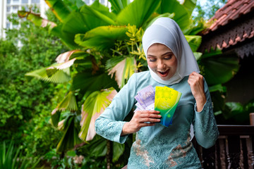 A portrait of young malay woman with surprise happy expression, holding an envelope of pocket money...