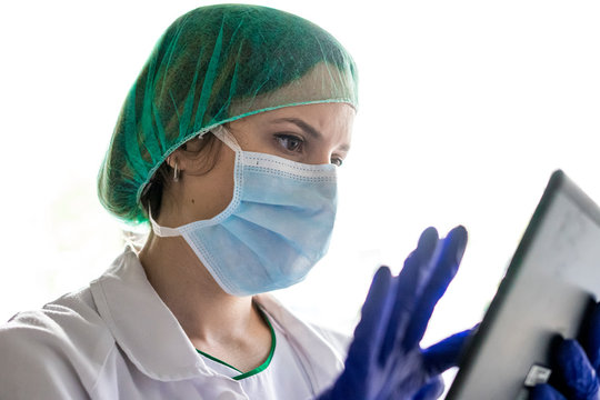 Cropped Shot Of An Unrecognizable Female Nurse Using A Digital Tablet While Standing In A Hospital. With A Mask