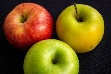 Three apples, one green and two red and yellow on a dark background
