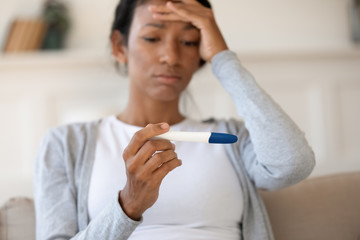 Obraz na płótnie Canvas Sad african american girl millennial hold pregnancy test in her hand. Upset by negative result, health problem or infertility concept, shocked about unwanted and unexpected pregnancy
