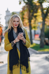 cute emotional attractive blonde woman in coat with smartphone walks the city street. communication during the walk, lifestyle, street.