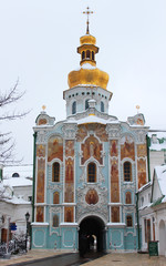 Fototapeta premium Medieval Gate Church of the Trinity of Kyiv Pechersk Lavra. View of east facade from the monastery side on a background of cloudy grey sky in winter. Soft focus