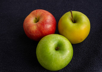 Three apples, one green and two red and yellow on a dark background