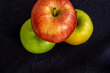 Three apples, one green and two red and yellow on a dark background