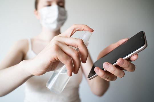 Cleaning mobile phone to eliminate germs, coronavirus Covid-19. Woman hands cleaning smartphone by alcohol hand sanitizer and wipe with cloth