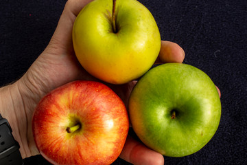 Three apples, one green and two red and yellow in the hand.
