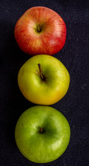 Three apples, one green and two red and yellow on a dark background
