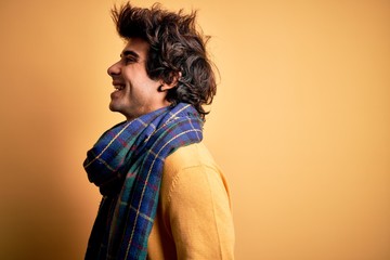 Young handsome man wearing casual scarf standing over isolated yellow background looking to side, relax profile pose with natural face with confident smile.