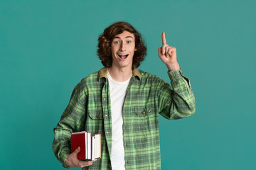 Excited young student with books and notebook having brilliant idea on color background