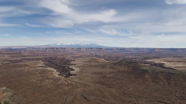 A wide timelapse lookout across Canyonlands National Park with clouds flowing over the distant La Sal Mountains.
