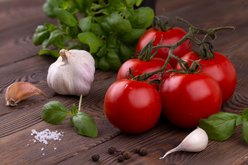 A branch of ripe red tomatoes, basil and garlic and spices on a wooden table in a rustic style. Organic food