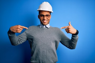 Young handsome african american engineer man with dreadlocks wearing safety helmet looking confident with smile on face, pointing oneself with fingers proud and happy.