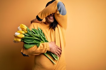 Young african american afro romantic man with dreadlocks holding bouquet of yellow tulips Smiling cheerful playing peek a boo with hands showing face. Surprised and exited