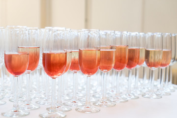Arrangement of many champagne glasses with pink champagne on a table with a white tablecloth