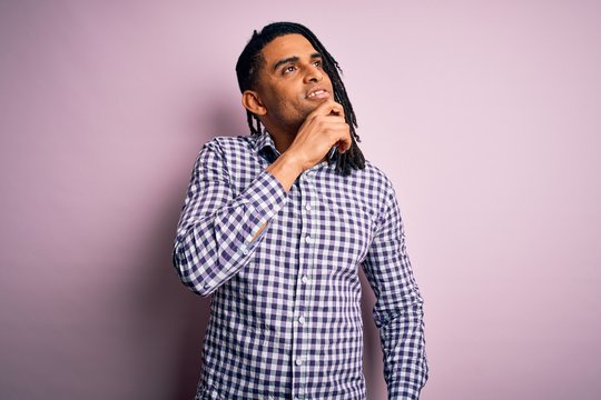 Young handsome african american afro man with dreadlocks wearing casual shirt with hand on chin thinking about question, pensive expression. Smiling and thoughtful face. Doubt concept.