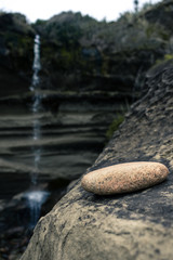 
Image of a stone resting on the hillside with the waterfall in the background taken on a cloudy day at Truman Track, New Zealand