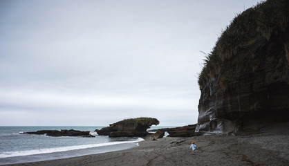 Gorgeous image of blonde toddler girl running down a pebbles beach taken on a cloudy winter day at Truman Track, New Zealand