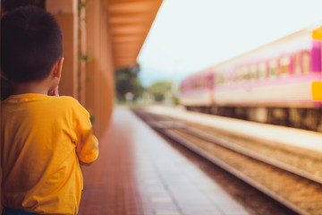 Little boy is looking the train at train station in summer. Travel concept.