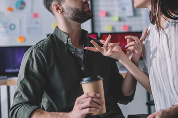 Cropped view of data analyst holding paper cup and talking to colleague
