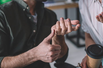 Cropped view of data analyst showing thumb up gesture to colleague with coffee to go