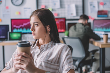 Data analyst holding coffee to go while colleague working in office