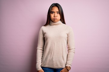 Young beautiful asian girl wearing casual turtleneck sweater over isolated pink background puffing cheeks with funny face. Mouth inflated with air, crazy expression.