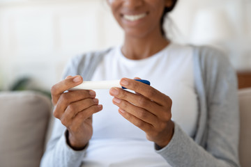 Close up of happy black girl smiling and hold pregnancy or ovulation test in hands. Desired, planned and successful pregnancy, rejoice and celebrate positive result, concept of health and motherhood - obrazy, fototapety, plakaty