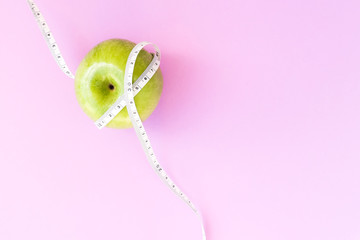 Diet concept. Green fresh apple with measuring tape on a pink background. Diet, programm, measuring tape, summer.