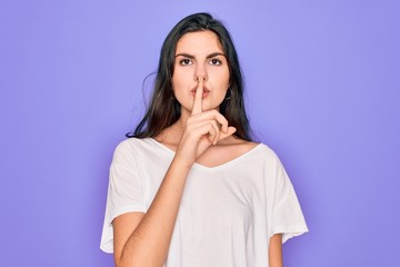 Young beautiful brunette woman wearing casual white t-shirt over purple background asking to be quiet with finger on lips. Silence and secret concept.