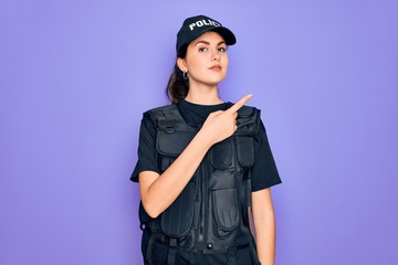 Young police woman wearing security bulletproof vest uniform over purple background Pointing with hand finger to the side showing advertisement, serious and calm face